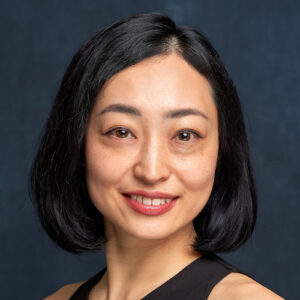 Closeup headshot of Japanese woman smiling and looking at camera. She has short black hair and is smiling while looking directly at camera.